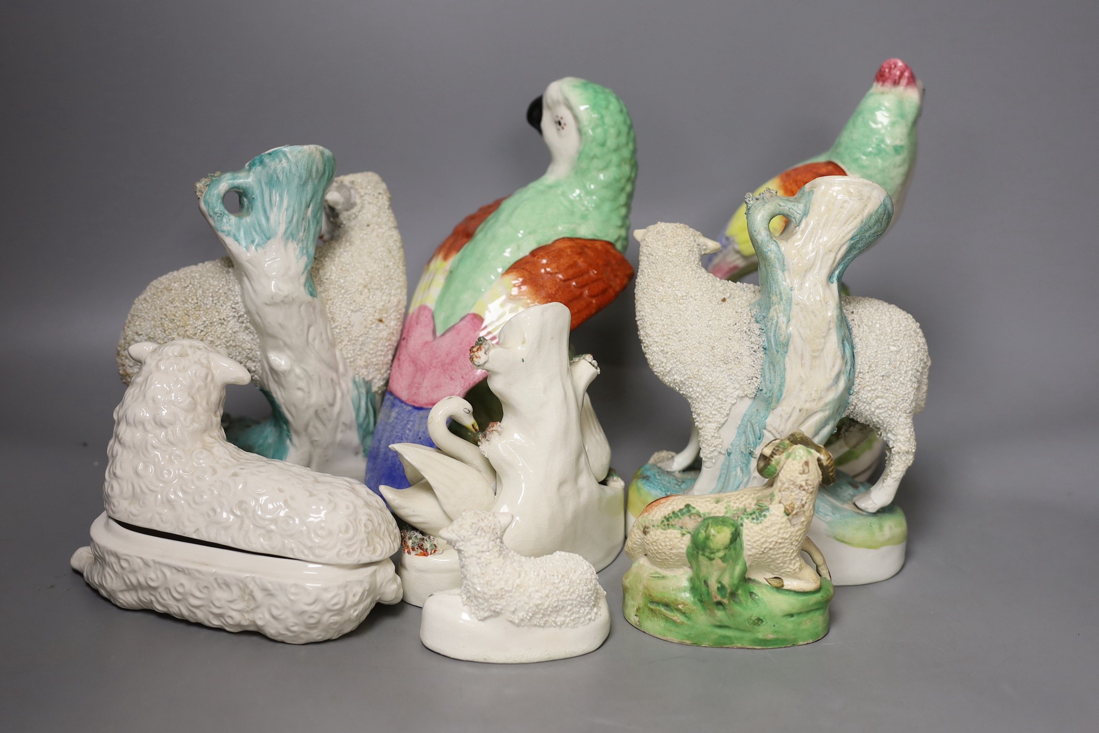 A group of Staffordshire animal and bird figures, to include a pair of sheep spill vases, two parrots, a swan spill vase, two further sheep and a cow and a continental pottery sheep tureen and cover - tallest 21.5cm